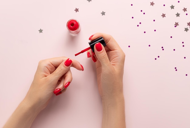 Woman painting her nails with red nail polish on pink background