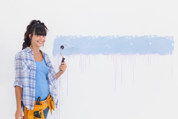 Woman painting wall blue and smiling at camera