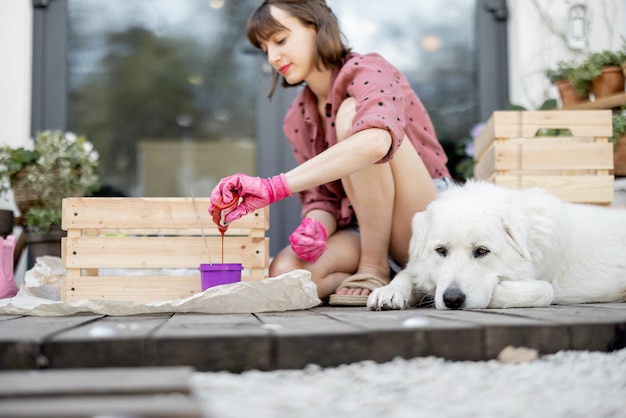 Woman painting wooden box sitting with dog on terrace