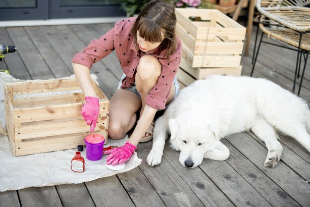 Woman painting wooden box sitting with dog on terrace