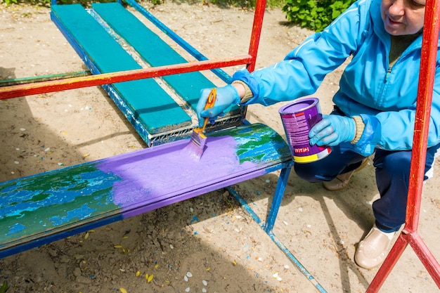 한 여자가 유치원 놀이터에서 벤치를 칠하고 있다