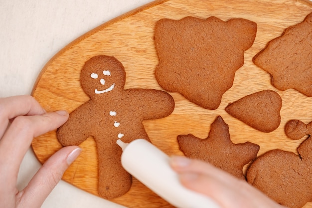 Foto la donna dipinge sul pan di zenzero al miele con glassa bianca per la pasticceria della colazione di natale