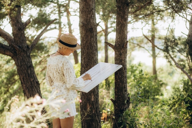 woman paints picture landscape girl artist view back summer park lake pond river denim shorts creating creativity artistic mood Blank white canvas getting started Brush color palette paints