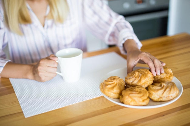 Foto donna in pigiama che beve caffè con pasticceria in cucina