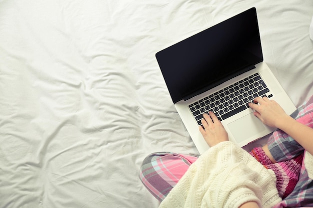 Woman in pajamas using a laptop on her bed