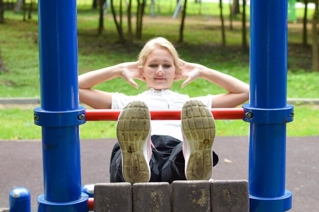 공원에 있는 여자는 체조에 종사하고 있습니다. 밖에 있는 수평 막대 체조에 있는 소녀