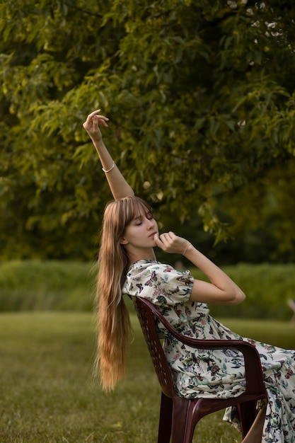 Donna in un parco si siede su una sedia nella foresta con lunghi capelli biondi. ragazze estetiche tenere