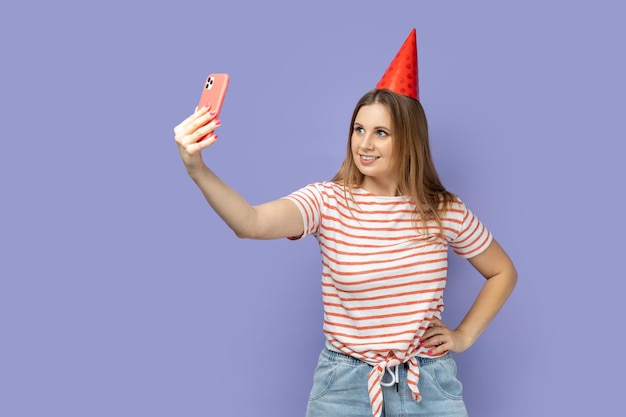 Woman in party cone broadcasting livestream or taking selfie for her blog keeps hand on hip