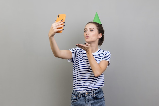 Woman in party cone taking selfie sending air kisses to followers having video call