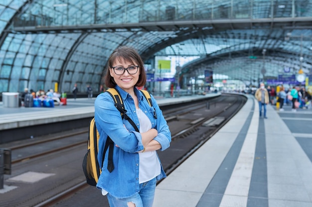 Woman passenger on railway platform inside station with crossed arms looking at camera