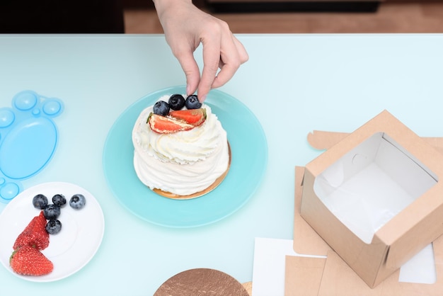 Woman pastry chef at home making finishing touches for homemade meringue cake Pavlova with summer fresh berries with selective focus Homemade pastry delicious sweets concept