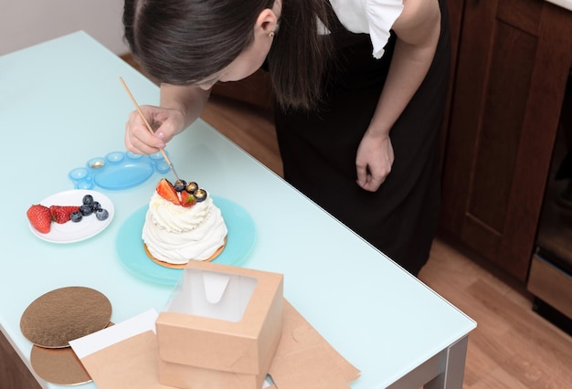 家庭で女性パティシエが手作りのメレンゲ ケーキの最後の仕上げを作る
