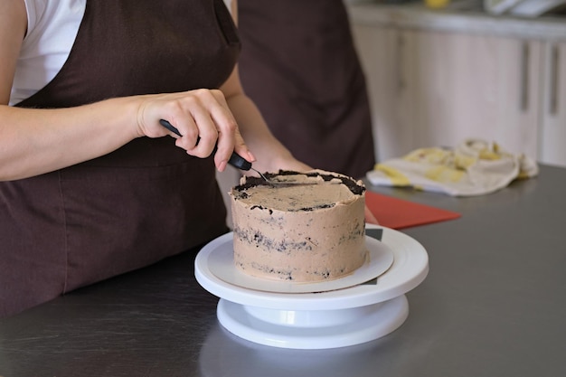 女性のパティシエがチョコレートケーキのクローズアップにチョコレートクリームを並べるケーキ作りのプロセス選択的な焦点