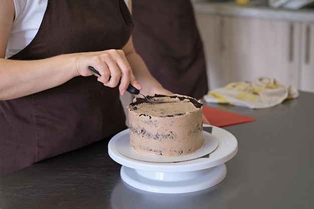 Woman pastry chef lines chocolate cream on chocolate cake closeup Cake making process Selective focus