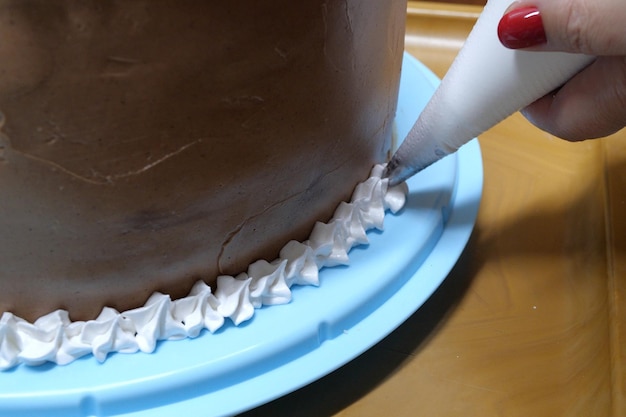 A woman pastry chef with a pastry bag in her hands squeezes cream on a cake in a home kitchen Professional chef at work on bakery kitchen culinary baking and cooking food concept home cooking