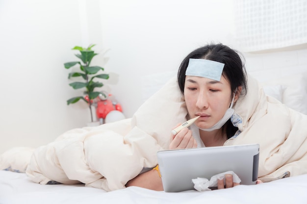 Woman patient examines body temperature during consultation\
with smart doctor. sick woman in bed video call to doctor using\
tablet. concept of home isolation telemedicine and patient\
counseling online