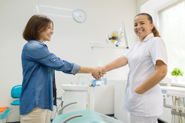 Woman patient shaking hand of female dentist having visit in medical clinic.