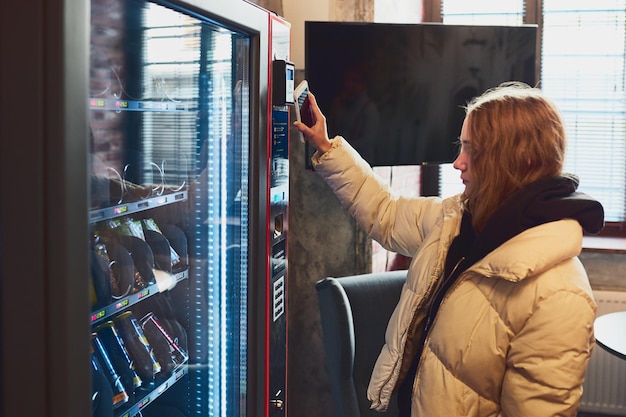 写真 携帯電話でコンタクトレス支払い方法を使用して自販機で商品を支払う女性