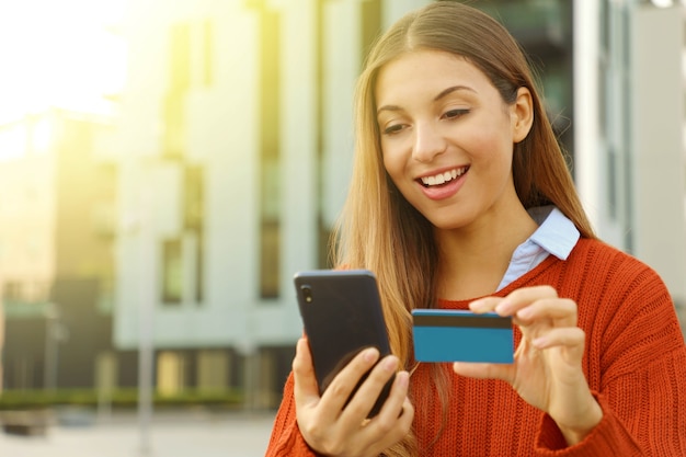 Woman paying online with smartphone and credit card outdoors