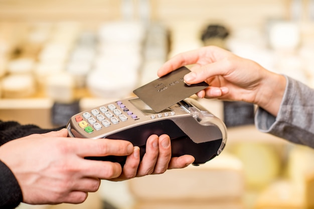 Woman paying with card contactless in the food store. Close-up view on the terminale and card