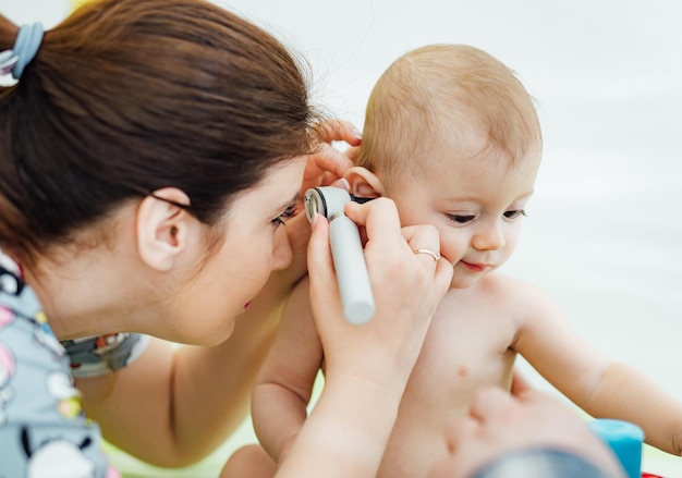 Woman pediatrician is examining little baby in clinic Baby's ear diagnosing