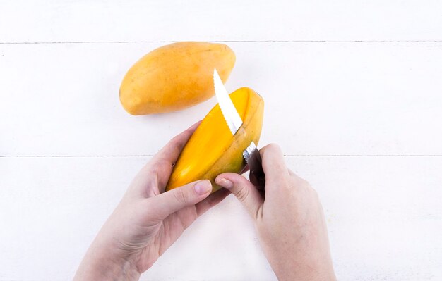 女性は白い背景の上のナイフでおいしい熟した黄色のマンゴーをはがします