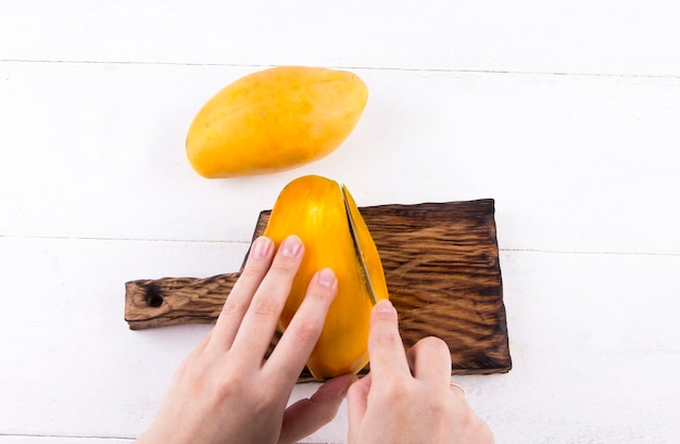 女性は白い背景の上のナイフでおいしい熟した黄色のマンゴーをはがします