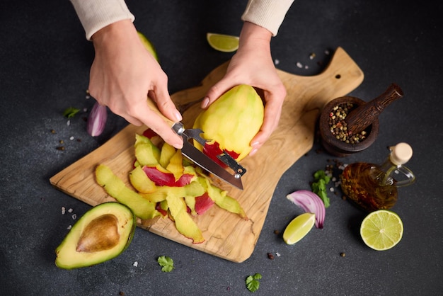 Foto donna che sbuccia il mango su una tavola da taglio in legno nella cucina domestica