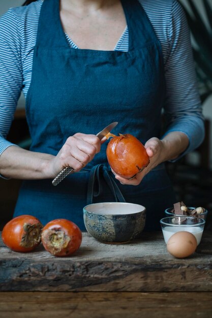 Woman peeling persimmon for preparing dessert, partial view