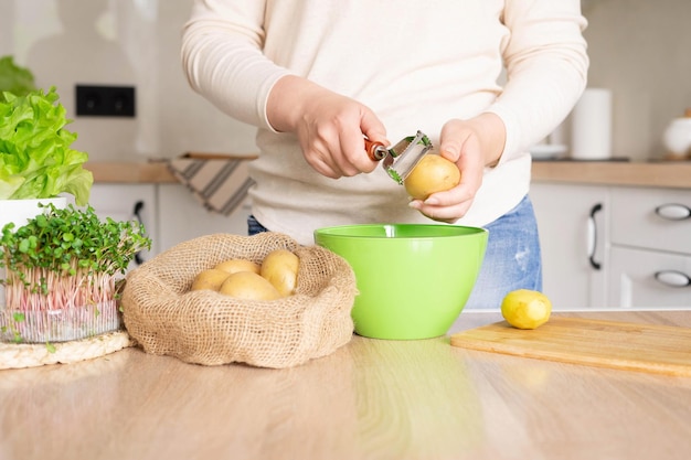 Woman peels potatoes with a vegetable peeler standing in the kitchen