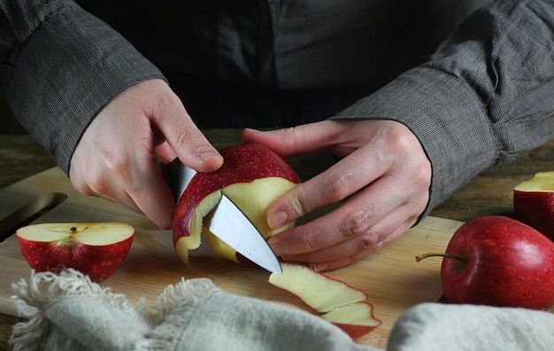Woman peels red apples. There is a board and apples on the table. There is a towel next to it.