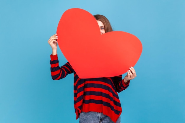 Woman peeping from big red heart being shy to express her romantic feelings and love