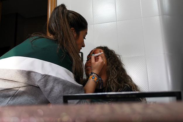 A woman performing Halloween makeup on a seated girl