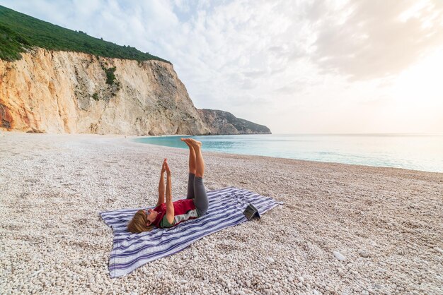 Foto donna che esegue esercizi di yoga su una bellissima spiaggia vuota in grecia drammatica costa panoramica baia scogliere rocciose nelle isole ionie