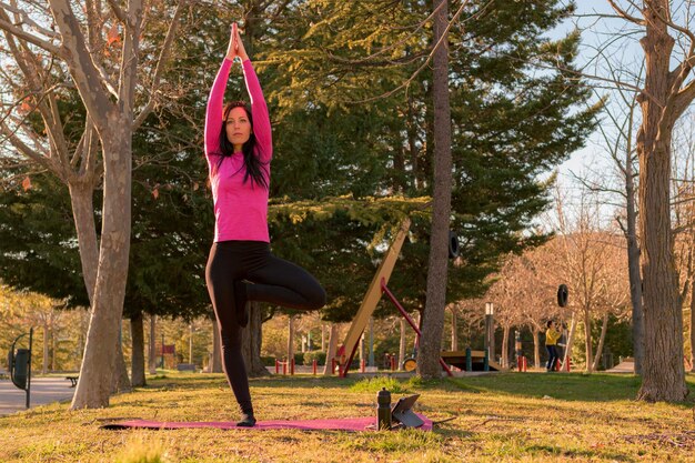 Woman performing yoga exercises in a park at sunset