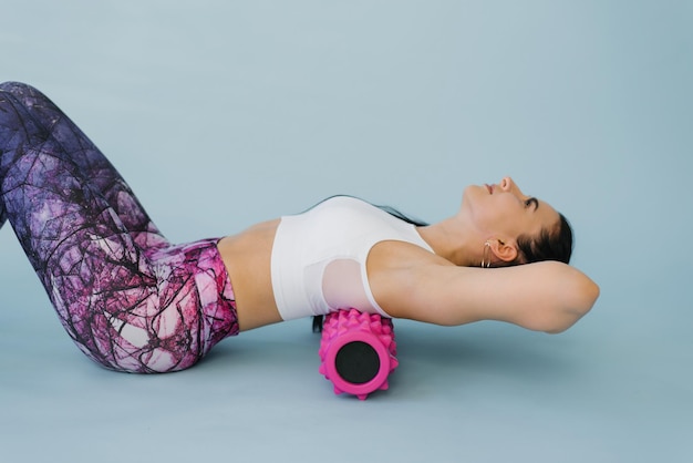 A woman performs myofascial relaxation of the hyperflexible\
muscles of the back with massage roller