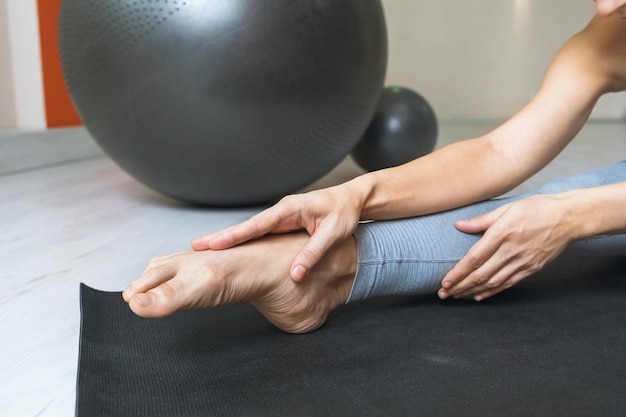 Woman performs a stretching of the muscles of the foot sits on\
a mat in the room