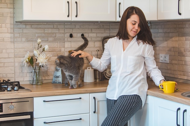 Woman pet the cat and drinking tea at the kitchen