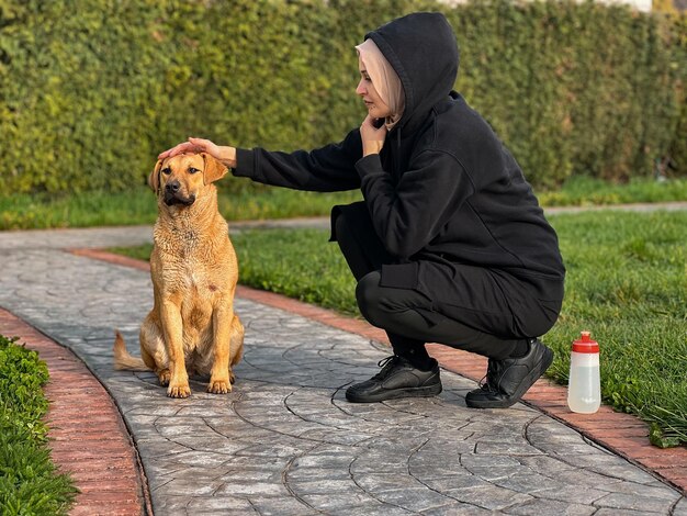 A woman petting a dog on a sidewalk