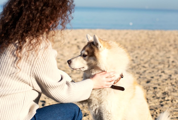 A woman petting a husky dog on the beach