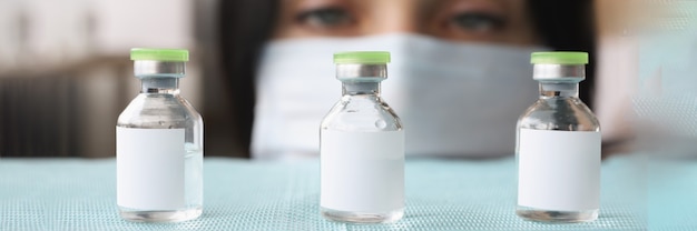 Woman pharmacist in protective medical mask selecting glass bottles with liquid closeup