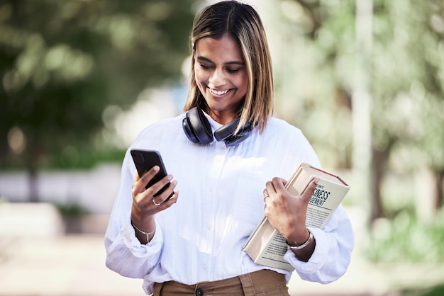 Woman phone or student with books in park outdoor for communication music or chat Social media research and a happy young female person in campus nature with a smartphone connection and education