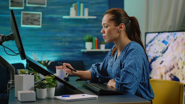 Woman photographer holding stylus and editing pictures using touch screen monitor at photography studio. Media editor retouching photos on computer app for image production. Photo retoucher