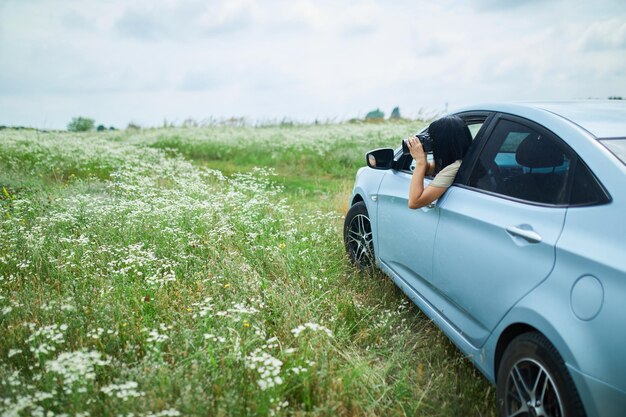 Woman photographer sitting in the car and photographing a flower field landscape, travel female take photo, space for text.