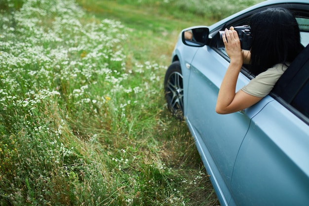 Woman photographer sitting in the car and photographing a flower field landscape, travel female take photo, space for text.