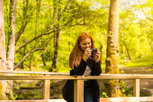 木製の橋で写真を撮る、秋の公園で楽しんでいる黒いジャケットを着た女性写真家