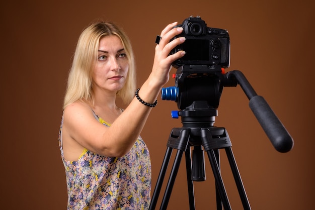 Женщина-фотограф с камерой DSLR в штативе в студии