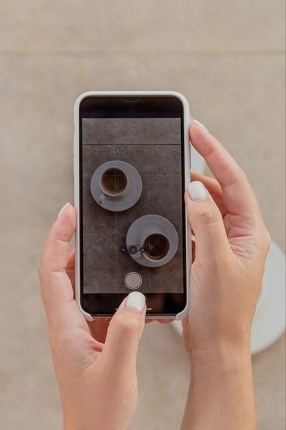 Woman photographing cups of coffee on smartphone