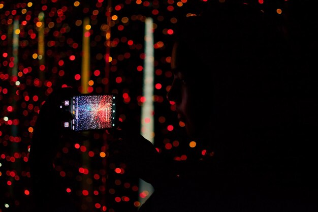 Woman photographing illuminated lighting equipment at night