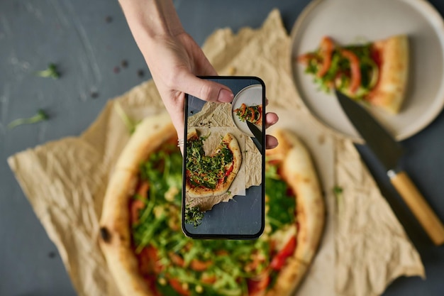 Woman photographing pizza on smartphone